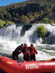 three people on a raft posing in front of a waterfall