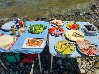 Deli style lunch spread on two pop up tables including tortillas, lettuce and condiments.